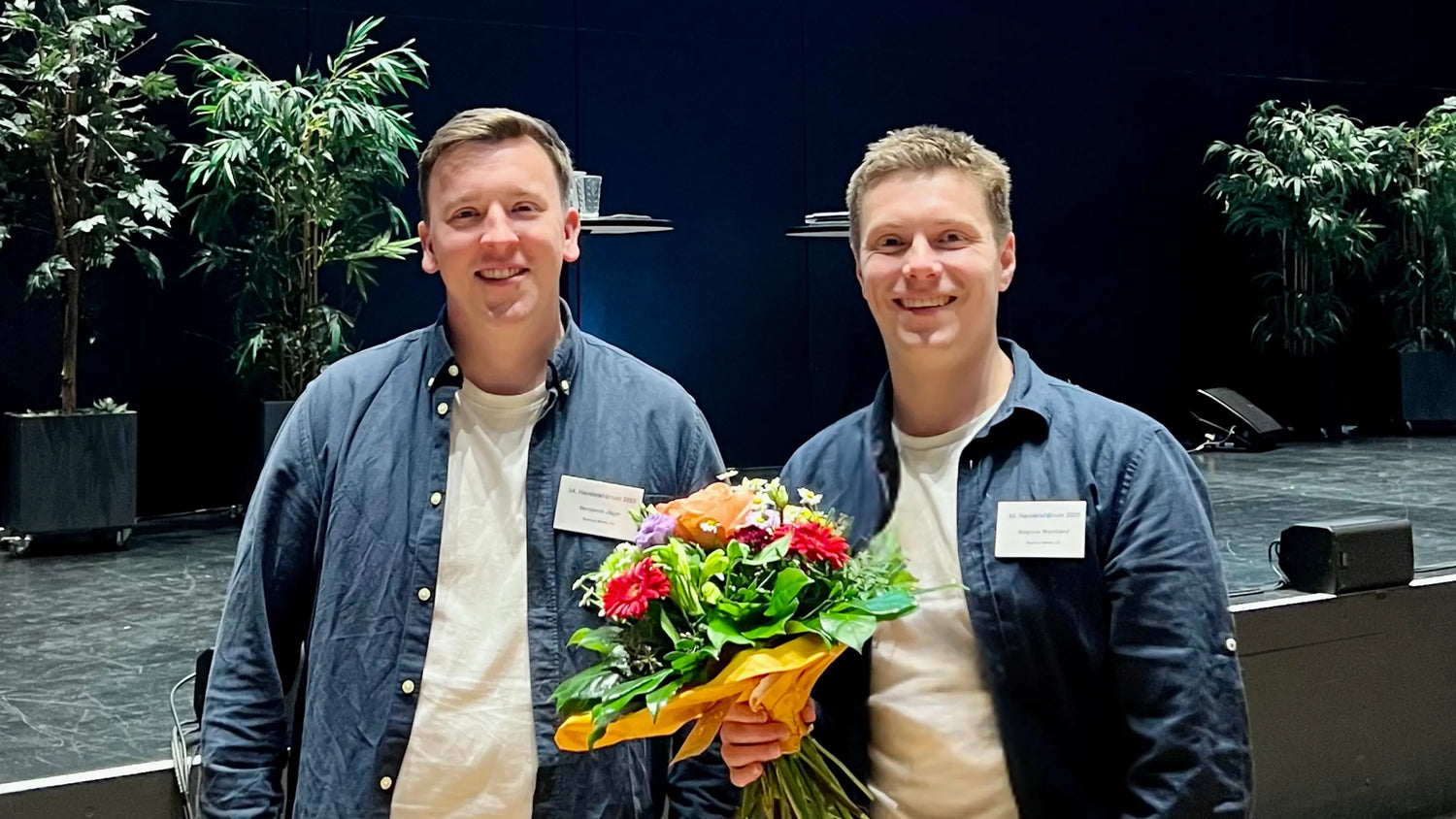 Foto von Magnus und Benjamin, die Gründer von Bennus Media, mit einem Blumenstrauß in der Hand