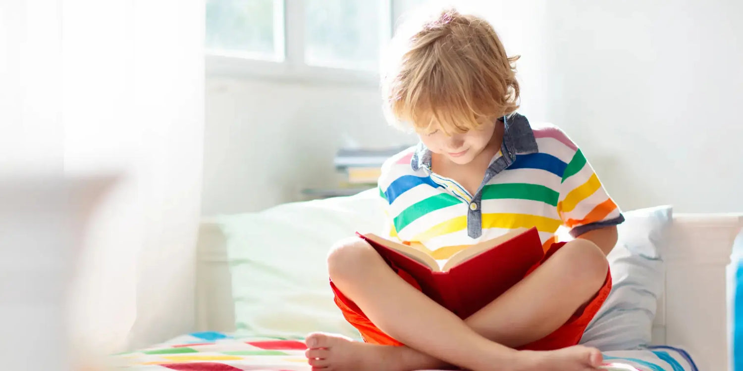 Kind sitzt im Schneidersitz auf einem Bett und liest ein Kinderbuch