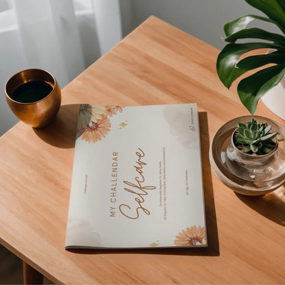 Foto vom Selfcare-Challendar, ein Mitmach-Jounal mit 30 Selfcare Challenges von Angelina Wenzler (muddivated) und Bennus Media für mehr Achtsamkeit, Selbstliebe und Dankbarkeit im Alltag auf einem Tisch.